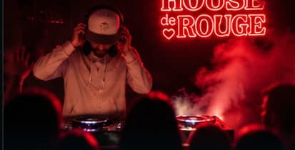 DJ mit Kopfhörern hinter den Decks vor roter Neonschrift, davor die Silhouetten der Gäste