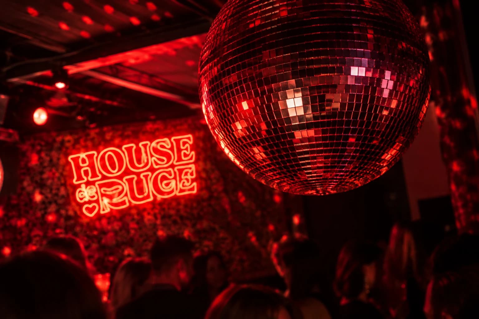 Discokugel im roten Licht neben der Neonschrift „House de Rouge“